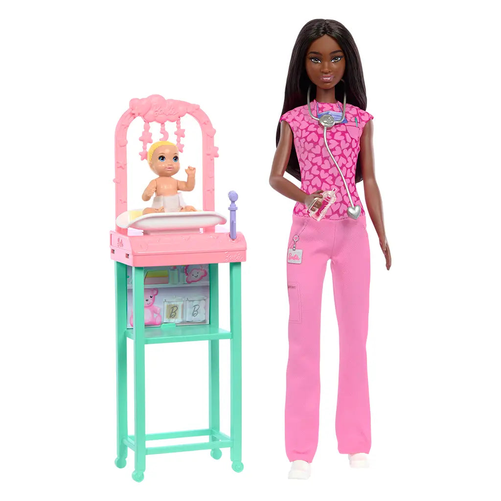 Barbie Baby Doctor brunette doll stands beside pink and teal nursery station holding baby doll, wearing stethoscope and scrubs, ready to care for her little patient.