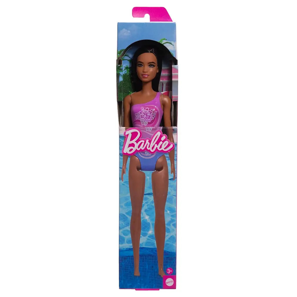 Barbie beach doll in original packaging, featuring long dark brown hair and a purple one-shoulder swimsuit with floral hibiscus print, displayed against a poolside backdrop.