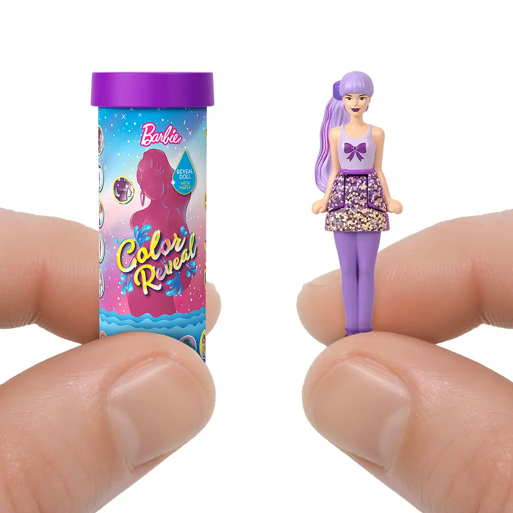 Hand holds Barbie Color Reveal mini doll beside decorated reveal tube, showing a revealed doll with purple hair, bow-print top, glitter skirt, and matching leggings for stylish play.