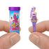 Hand holds Barbie Color Reveal mini doll beside decorated reveal tube, showing a revealed doll with purple hair, bow-print top, glitter skirt, and matching leggings for stylish play.