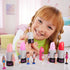 Smiling child holding Barbie lipstick tube toy with mini doll revealed, surrounded by multiple colorful lipstick tubes and collectible dolls on a table.