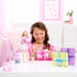 Smiling girl in pink plays with Barbie Party Unboxed set, unwrapping colorful gift boxes while Barbie doll, pet dog, and birthday cake accessories sit on white table.