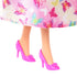 Barbie doll close-up shows glossy pink high-heeled shoes with small floral accents, peeking beneath a satin skirt printed with colorful butterflies on a soft pastel background.