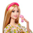 Close-up of Barbie doll wearing a lemon-print robe and pink headband, smiling while holding a pink facial massager accessory near her cheek.