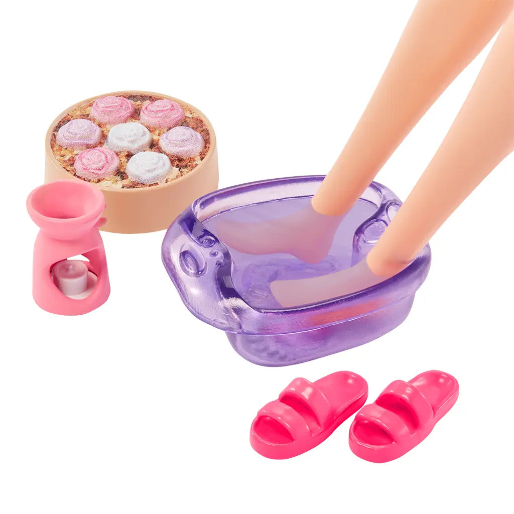 Barbie spa set accessories including purple foot bath, pink sandals, rose-shaped bath bombs, and small pink aromatherapy holder for doll play.