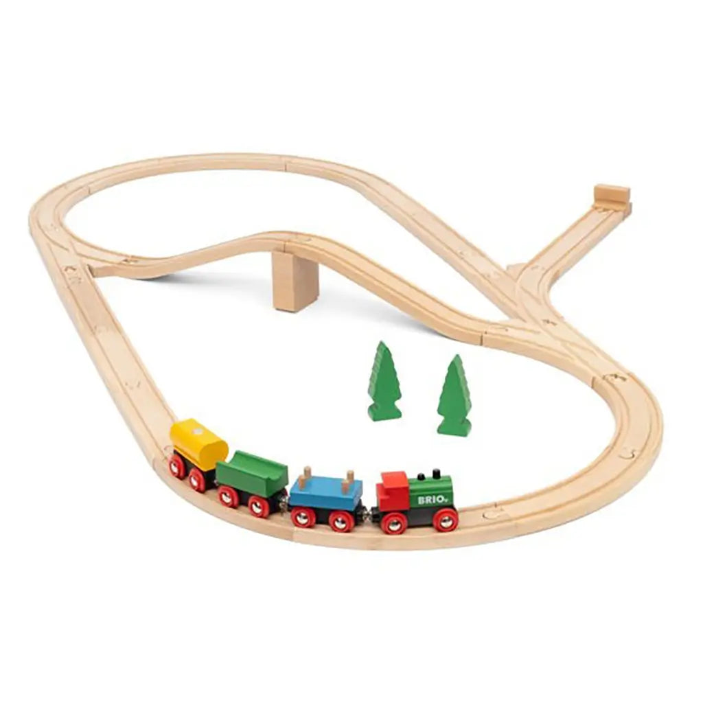 BRIO 65th Anniversary Train Set assembled with wooden track, bridge, green and red locomotive, colorful wagons, and two green tree accessories on a white background.