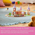 BRIO Disney Princess Castle set placed on a rug, showing pink train with princess figures riding through pastel castle towers, wooden track, and small tree accessory.