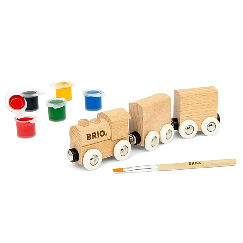 BRIO Paint Train kit components arranged with a wooden locomotive, two blank train cars, five paint pots in primary colors, and a branded wooden paintbrush.