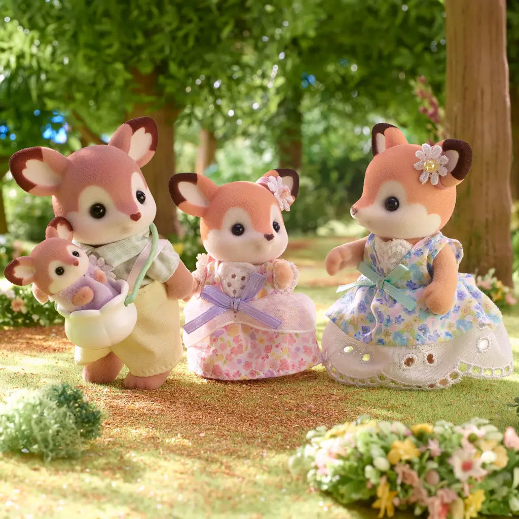 Calico Critters Deer Family figurines posed in a forest scene, with the father carrying the baby in a pouch, while the mother and child deer wear pastel floral dresses.