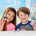 Calico Critters Seal Family toys shown with a smiling boy and girl, each holding plush seal figures dressed in blue and pink outfits, posed indoors with bright window light.