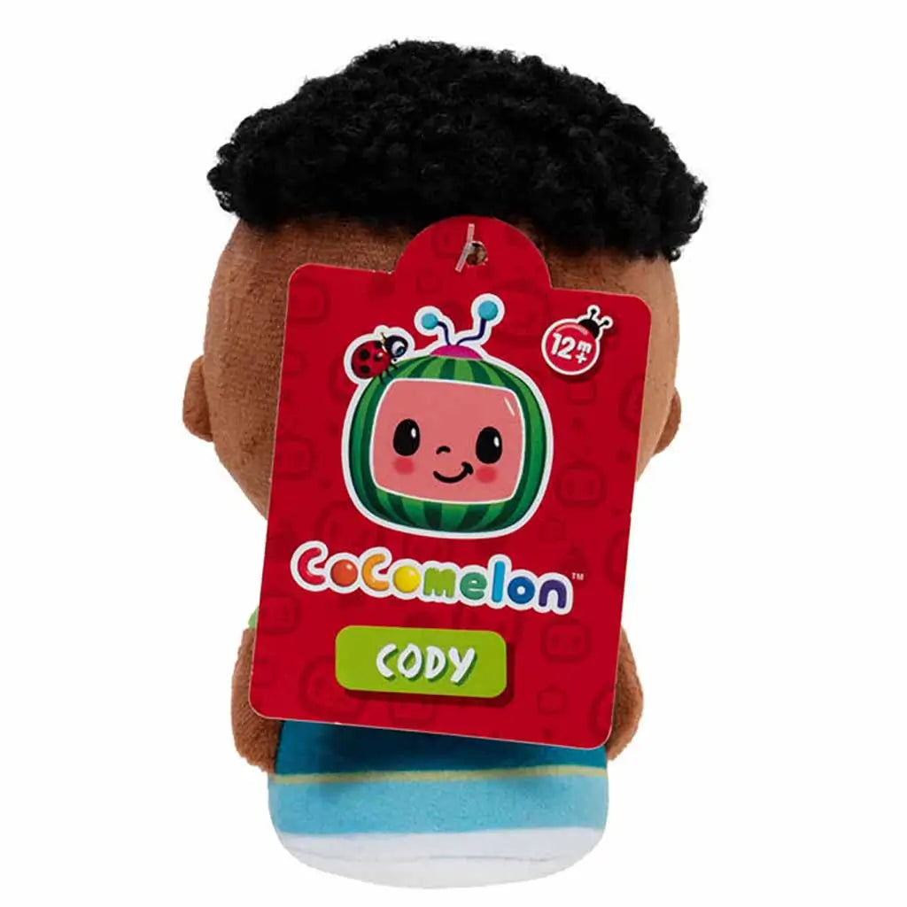Back view of CoComelon Cody 5-inch plush showing the red CoComelon tag with smiling watermelon logo, ladybug, and name label, attached to the soft toy designed for ages twelve months and up.
