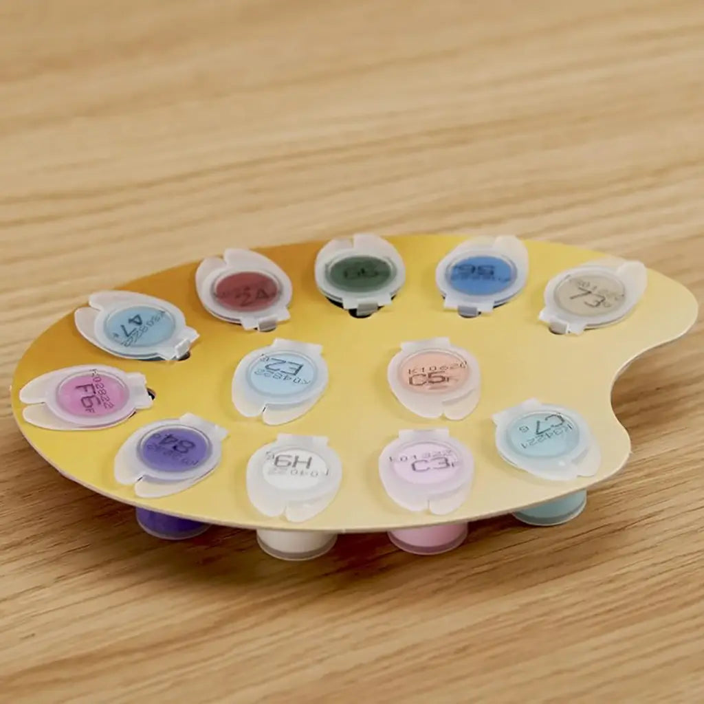 Yellow plastic palette holding multiple small acrylic paint pots in pastel and bold colors with numbered lids, neatly arranged on a wooden table for organized painting sessions.