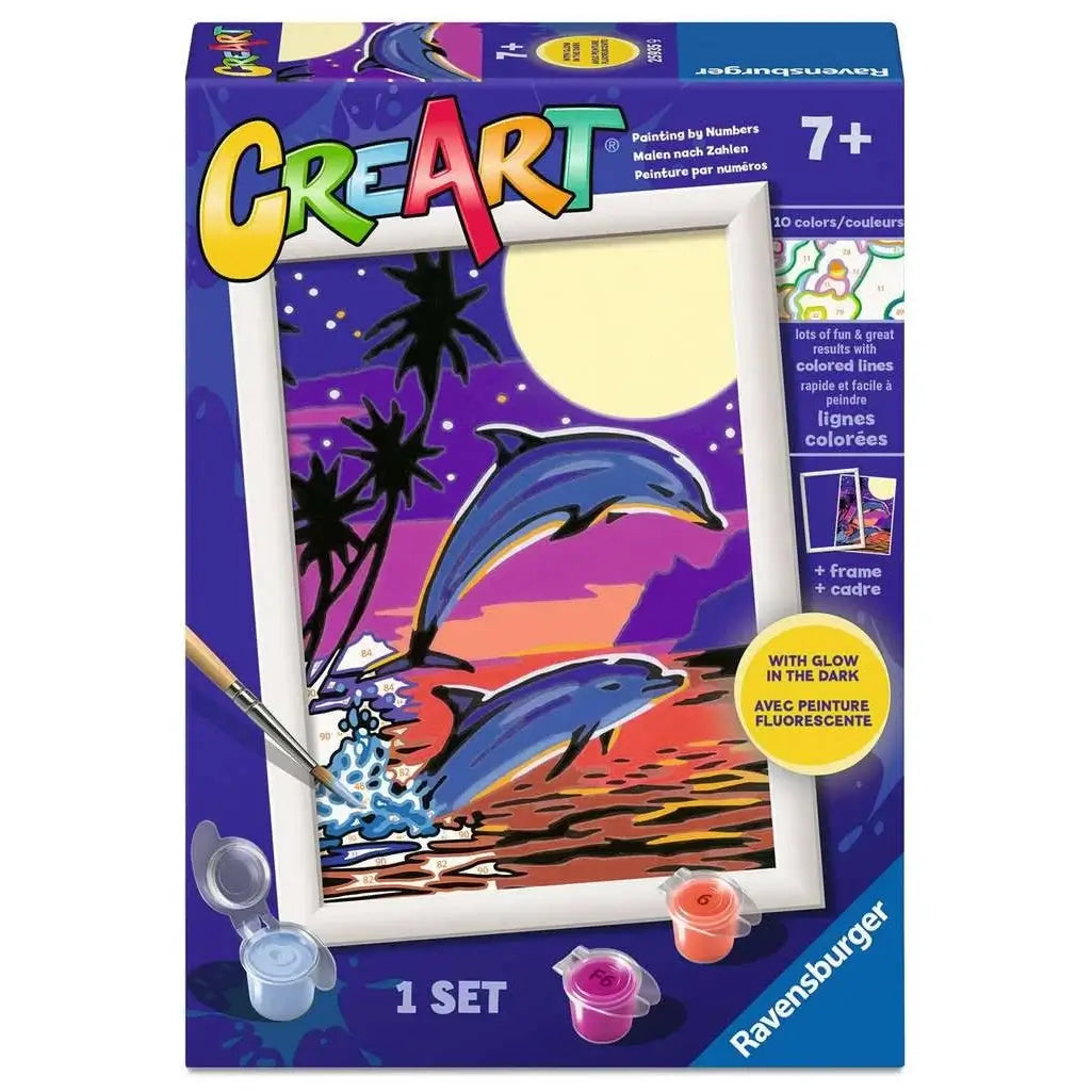 Front of Ravensburger CreArt paint-by-numbers kit for kids ages 7+, featuring glow-in-the-dark dolphins jumping over ocean waves at sunset with included paints.