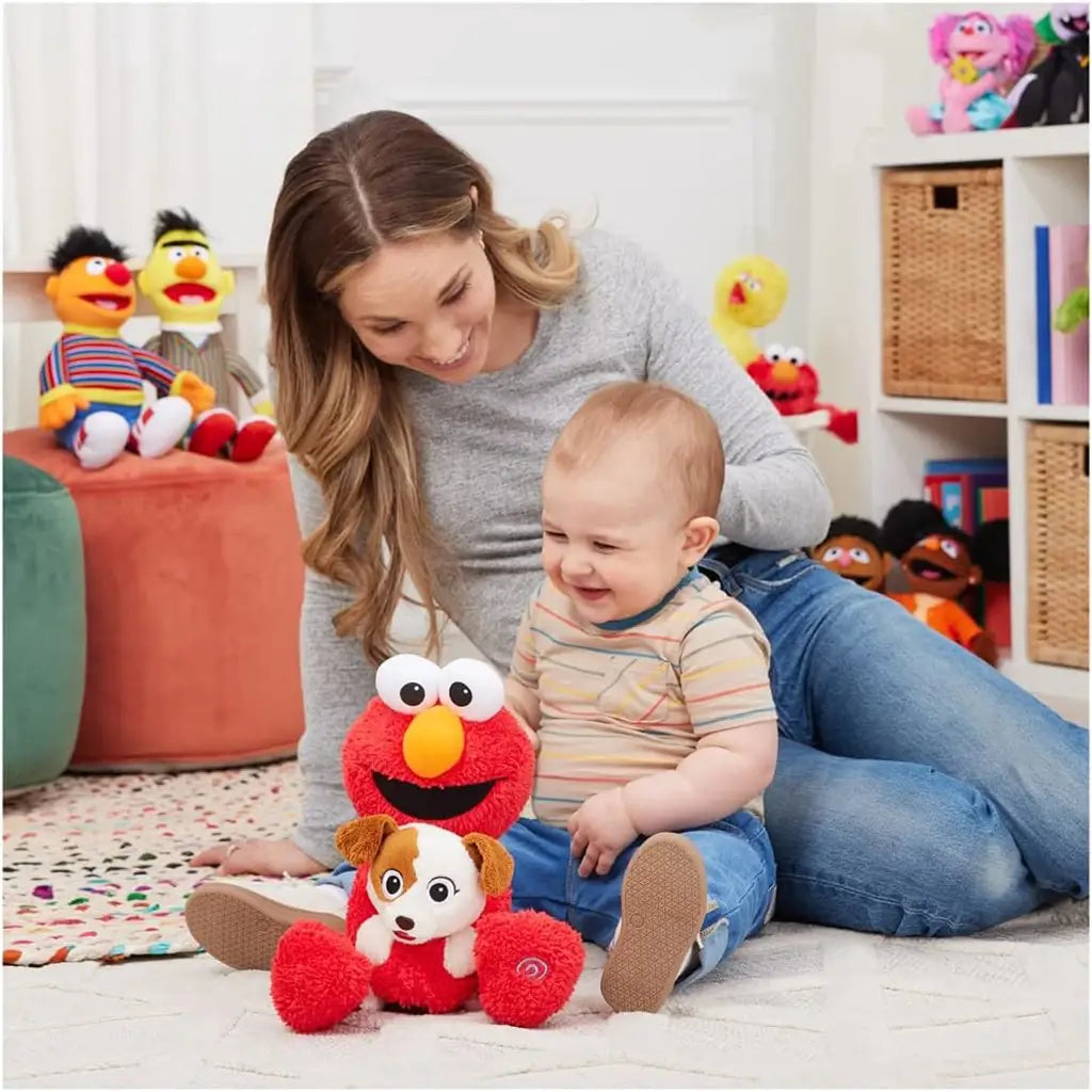 Smiling mother and baby on carpet playing with plush Elmo hugging Tango dog, surrounded by colorful Sesame Street toys, showing fun and family bonding moment.