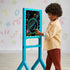 Young child drawing on the Discovery Glow Easel standing art board, creating a neon astronaut design on the illuminated surface in a playroom with colorful wall patterns.
