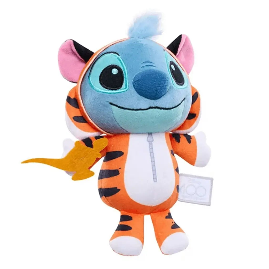 Soft Disney Stitch plush wearing an orange and black tiger-striped Rajah onesie with large teal eyes and a playful smile, clutching a golden lamp prop, photographed on a plain white surface.