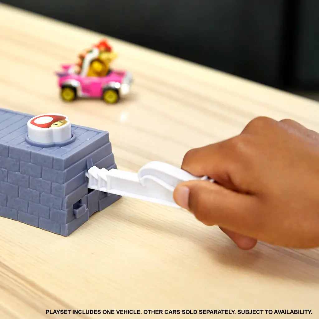 A child’s hand launches a Hot Wheels Mario Kart car from gray stone-look ramp with red mushroom launcher, sending vehicles racing into Boo’s Spooky Sprint haunted track.