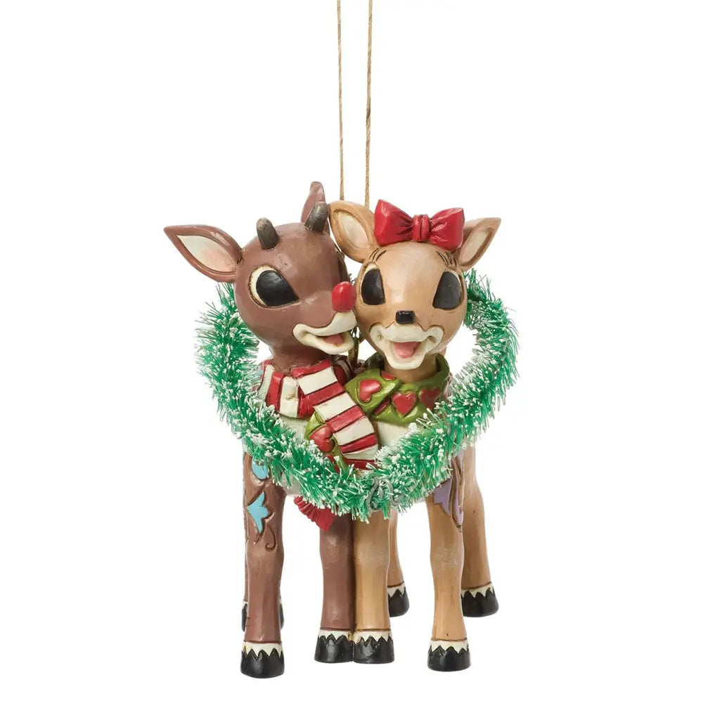 Front view of Jim Shore Rudolph and Clarice ornament, showing smiling reindeer with festive scarves inside a heart-shaped green tinsel wreath.