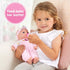 Young girl in a white shirt sits on a chair feeding her Kidoozie Sweetie Doll with a pink baby bottle, demonstrating nurturing playtime.