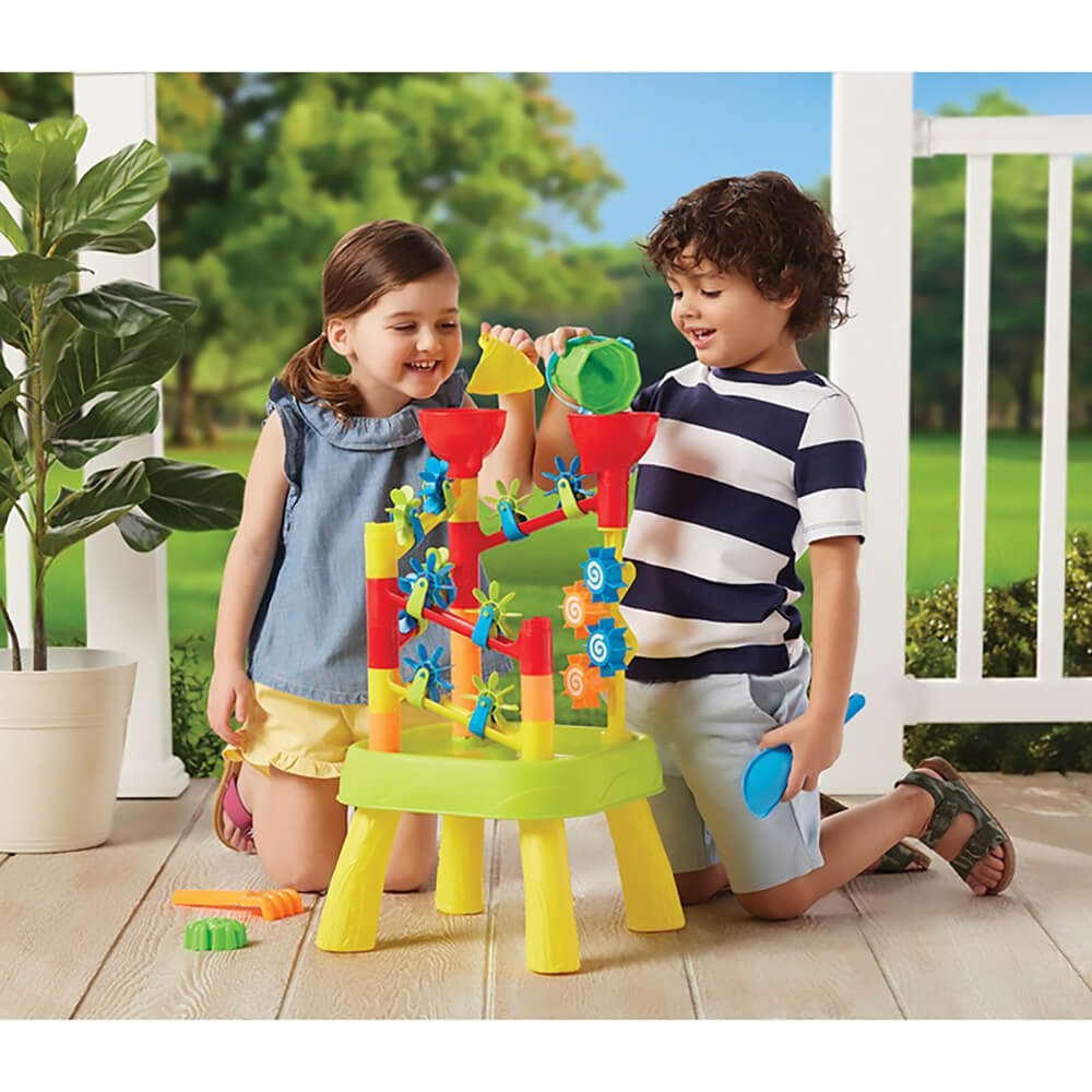 Two young children play with the Kidoozie Water Tower Playset on a porch, pouring water into colorful funnels that spin blue and orange water wheels on a yellow table.