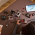 Overhead view of a person building LEGO Wednesday Morticia’s Cottage set with modular rooms, car pieces, and minifigures laid out beside a tablet displaying digital instructions.