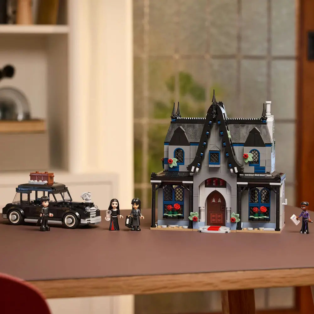 Completed LEGO Wednesday Morticia’s Cottage displayed on a table, showing the dark mansion, Addams family car, and four minifigures arranged for play.