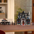 Completed LEGO Wednesday Morticia’s Cottage displayed on a table, showing the dark mansion, Addams family car, and four minifigures arranged for play.