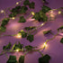 Faux ivy fairy light string featuring green leaves and small warm LED bulbs glowing softly against a purple background, part of the 3C4G room decor set.