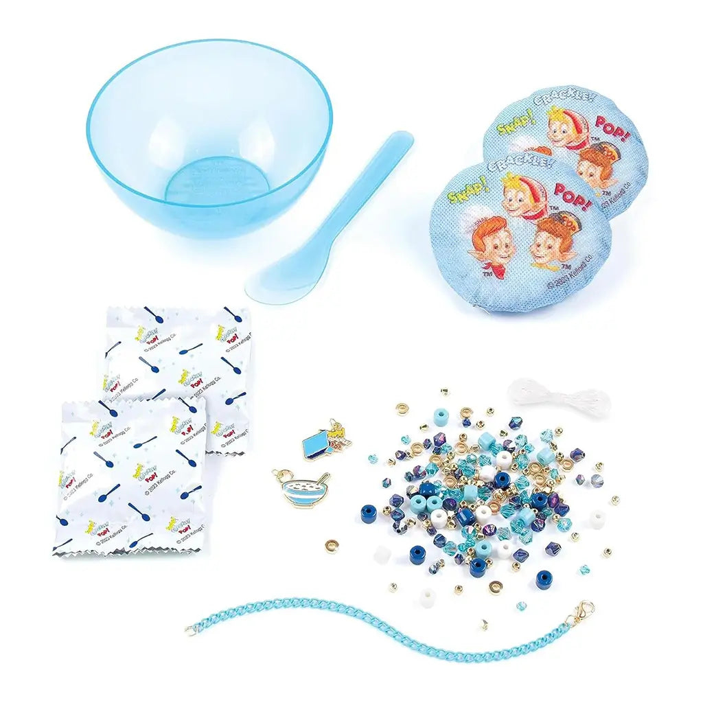 Rice Krispies DIY Bracelet Kit contents including blue bowl, spoon, dissolvable pouches, assorted blue and gold beads, string, and enamel charms shaped like cereal and milk.