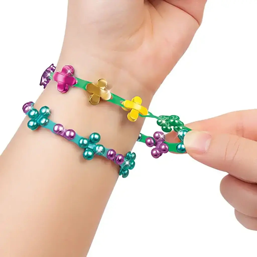 Close-up of a person’s hand linking colorful Linxo bracelets made of teal, gold, and purple plastic flower-shaped pieces, demonstrating the flexible interactive jewelry design system.