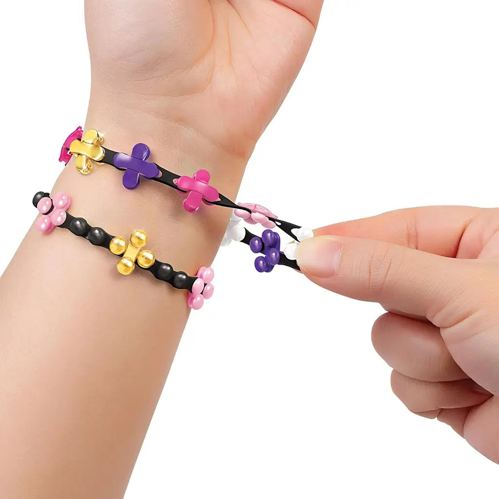 Close-up of hands stretching black and pink Linxo bracelets with purple, white, and gold floral connectors, demonstrating the flexible and reversible design feature of the jewelry set.