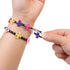 Close-up of hands stretching black and pink Linxo bracelets with purple, white, and gold floral connectors, demonstrating the flexible and reversible design feature of the jewelry set.