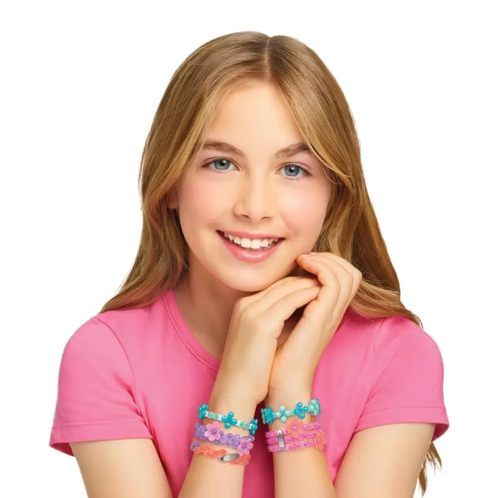 Smiling girl in a pink shirt wearing handmade Linxo Seaside Style bracelets in teal, purple, and coral colors, posing with hands under her chin against a white background.