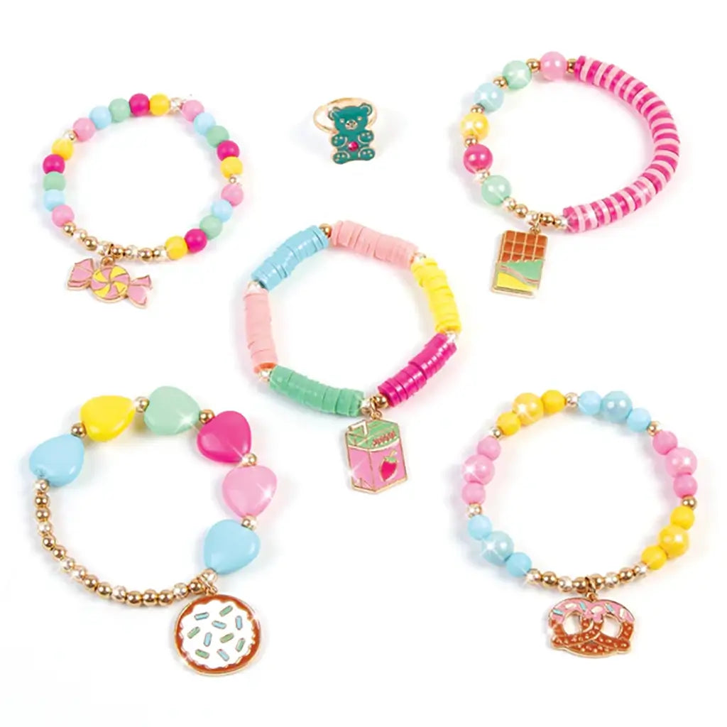 Five completed Make It Real Snackers bracelets with colorful beads and cute dessert-shaped charms like candy, chocolate, and pretzels displayed on white surface.