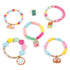 Five completed Make It Real Snackers bracelets with colorful beads and cute dessert-shaped charms like candy, chocolate, and pretzels displayed on white surface.