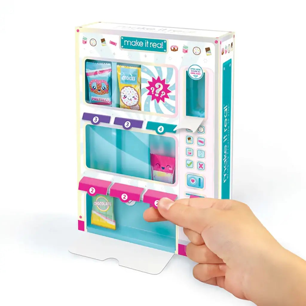 Hand pulling a lever on the Make It Real Snackers Bracelet Kit vending machine to release a mini snack-themed bracelet pack, promoting interactive DIY play.