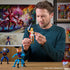 Person holding She-Ra action figure with sword and red cape, surrounded by other Masters of the Universe toys, in a colorful indoor display scene.
