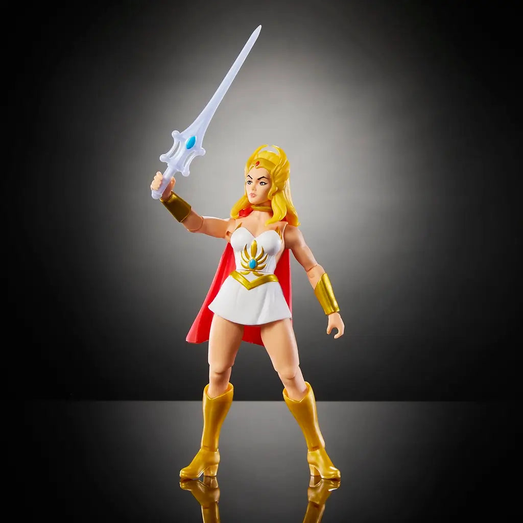 She-Ra Masters of the Universe figure holding silver sword aloft, dressed in white skirt with gold accents, red cape, and gold boots, standing on reflective black background.