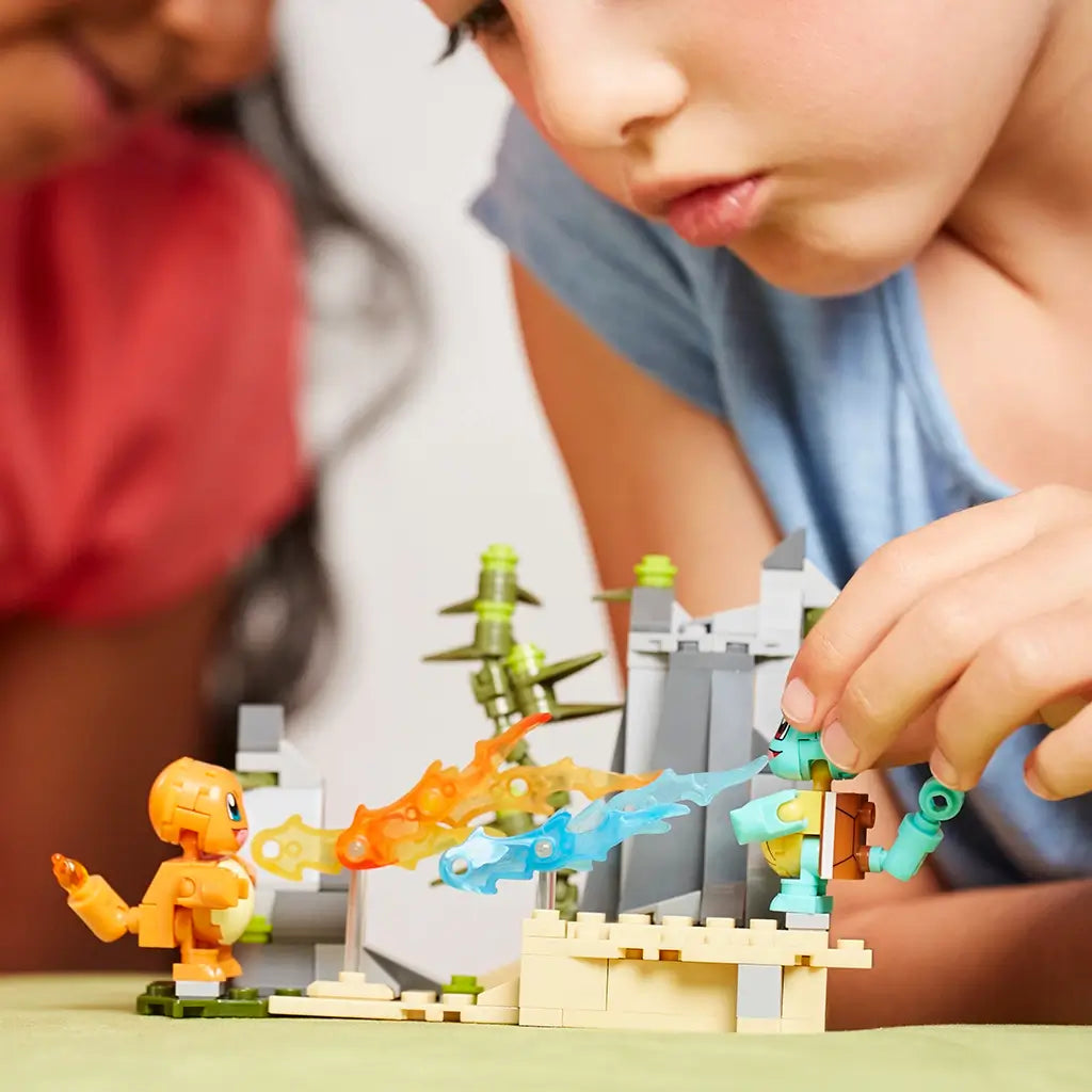 A child plays with Mega Construx Pokémon Squirtle and Charmander figures on a rocky battle arena, launching fire and water effects for an interactive build experience.