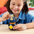 Smiling child in denim shirt playing with Mega Pokémon Mimikyu figure, placing it into the black Poké Ball toy on a wooden table in a bright indoor setting.