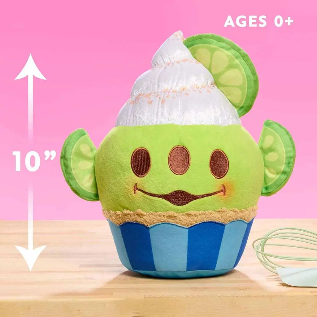 10-inch Disney Munchlings Toy Story Alien lime cupcake plush displayed on a wooden surface with a pink background, showing green body, white swirl top, lime slice ears, and text for ages 0 and up.