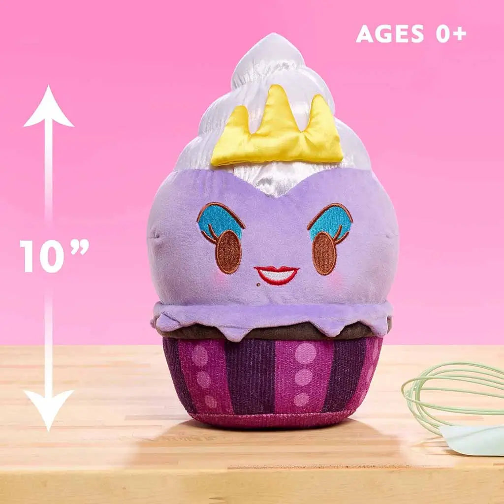 10-inch Disney Munchlings Ursula plush from The Little Mermaid shown against a pink backdrop with a height arrow and text for ages 0+, displaying its purple cupcake base and yellow satin crown.