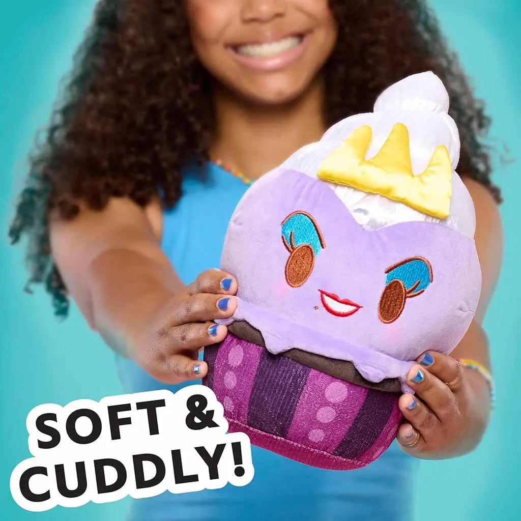 Disney Munchlings plush toy styled as Ursula from The Little Mermaid in a lavender cupcake design with blue eyeshadow, red lips, and a golden crown, held by a smiling girl with a turquoise background.