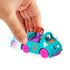 Hand pushing Polly Pocket teal dinosaur car with red-haired doll in the front seat and purple brontosaurus in the back, pink wheels rolling forward on a white background with motion blur.
