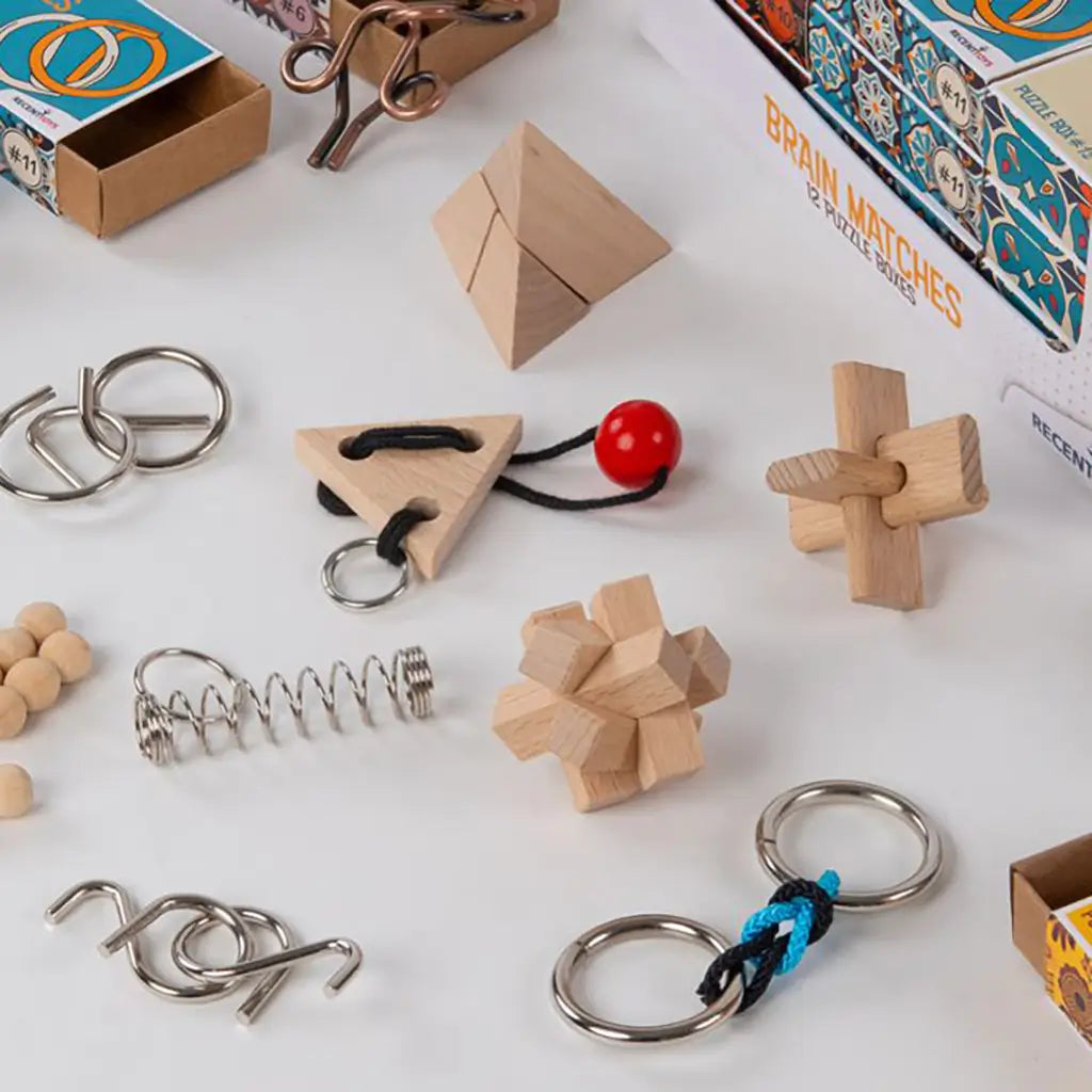 Set of wooden, metal, and rope brain teaser puzzles, including geometric blocks, rings, and spring pieces, arranged beside open matchbox-style puzzle boxes.
