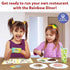 Two young girls smiling while playing with Skillmatics Rainbow Diner magnetic playset, arranging colorful pretend foods and play money on plates during imaginative restaurant playtime.