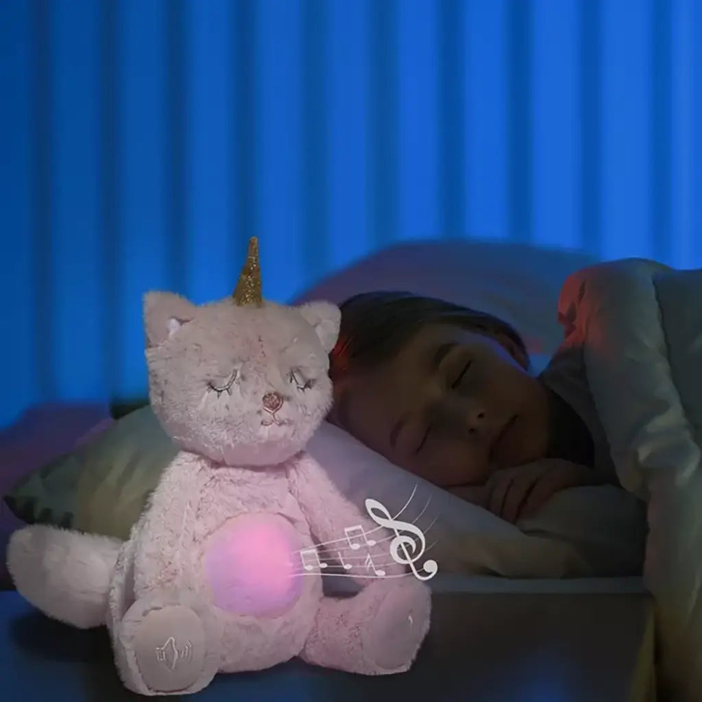 Child sleeping peacefully beside glowing pink unicorn cat plush toy with golden horn and music notes, creating a soothing bedtime scene.