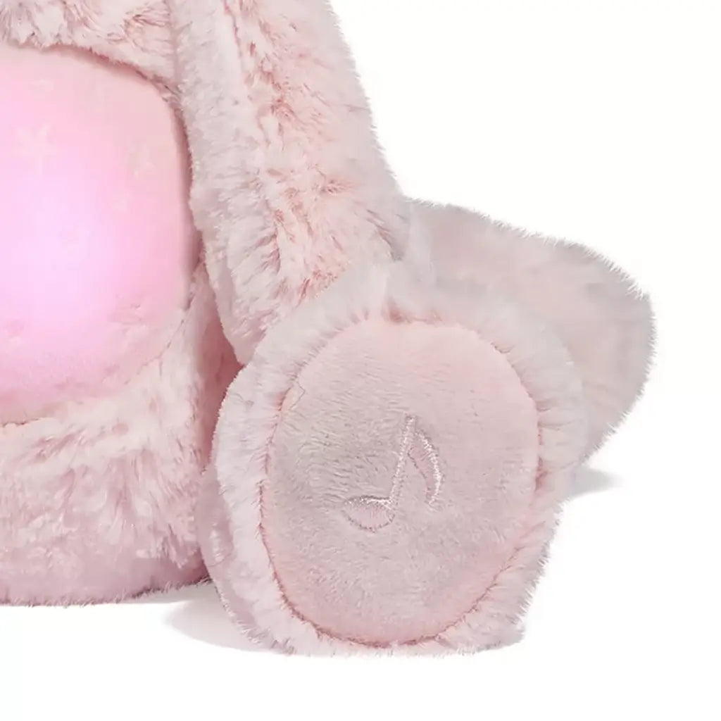 Detail of plush unicorn cat paw showing embroidered speaker icon on light pink surface, indicating sound control functionality.