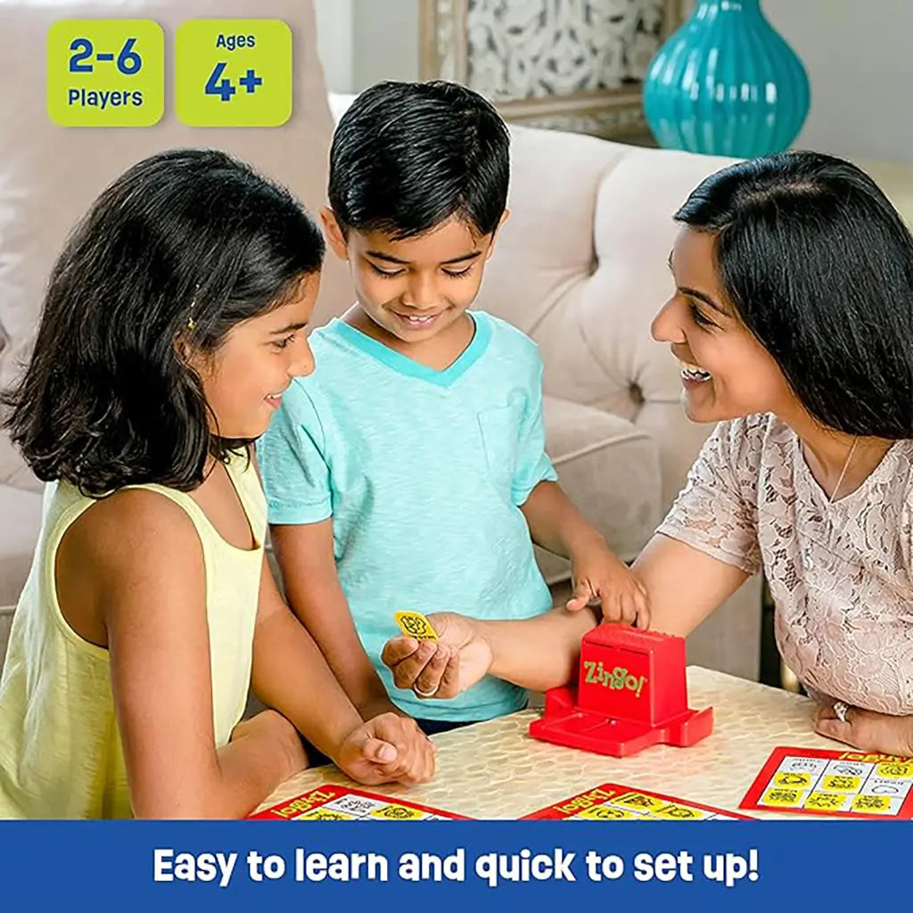 Parent and two children happily playing ThinkFun Zingo board game at home, with red Zinger machine and tiles, promoting word recognition, concentration, and family fun.