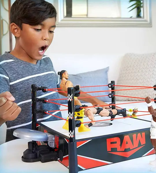 A young boy excitedly plays with WWE wrestling action figures in a RAW-branded toy wrestling ring, recreating an intense match